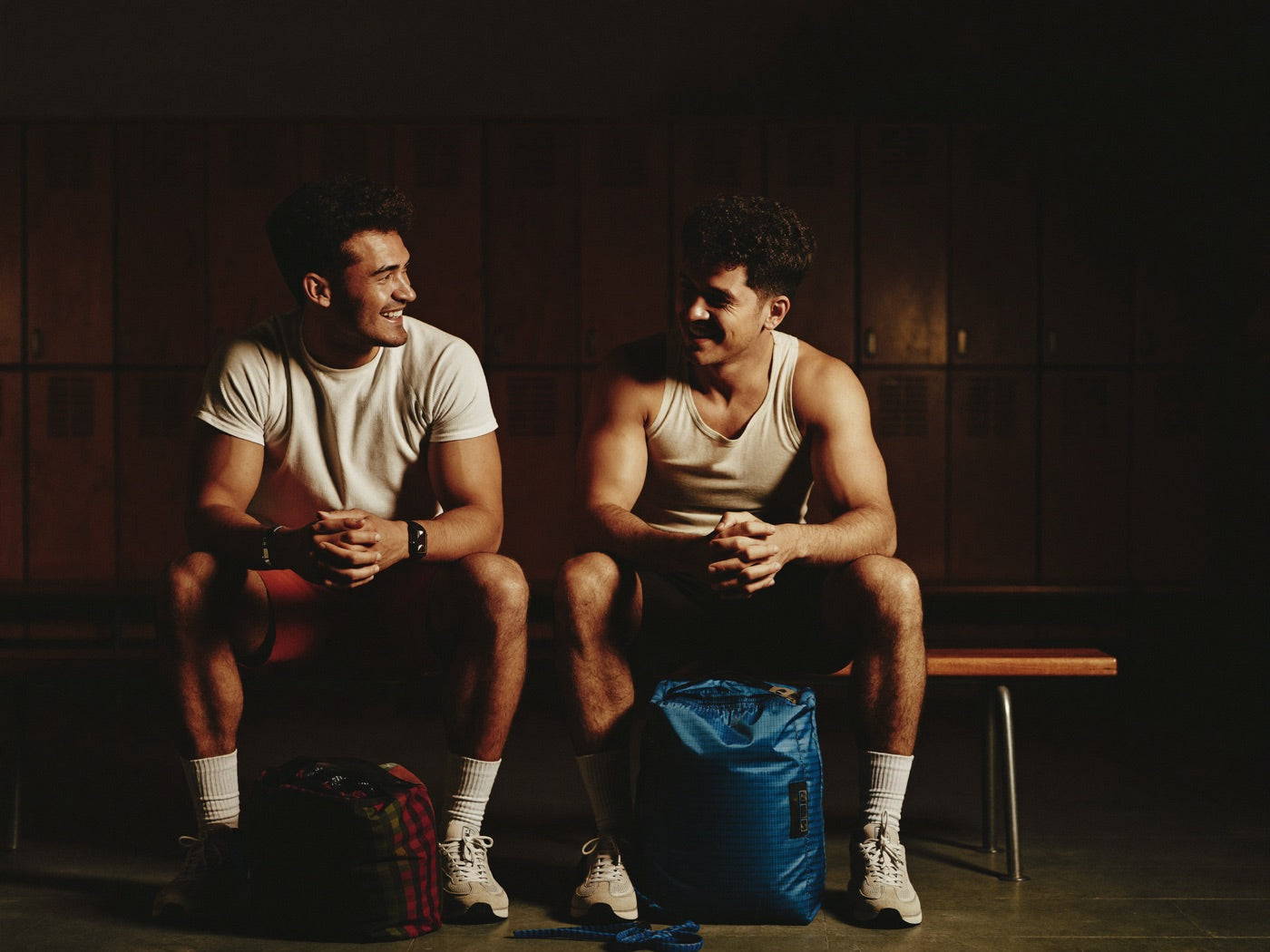 Two men laughing together on a bench in a moody gym locker room