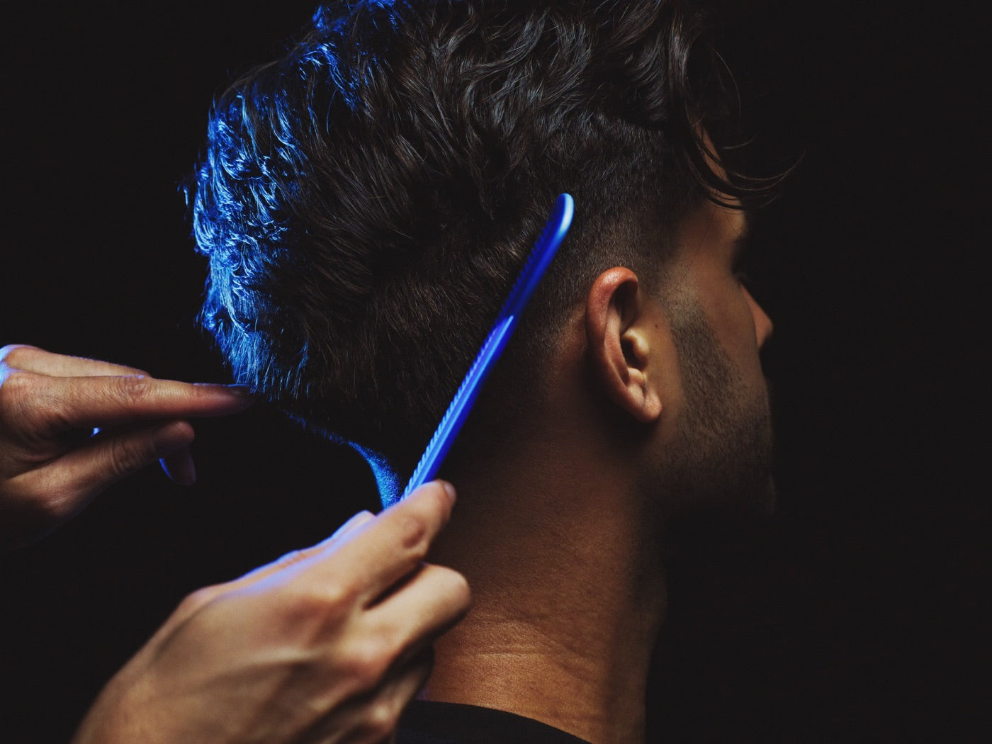 Barber combing a man's thick hair under blue-edged studio light