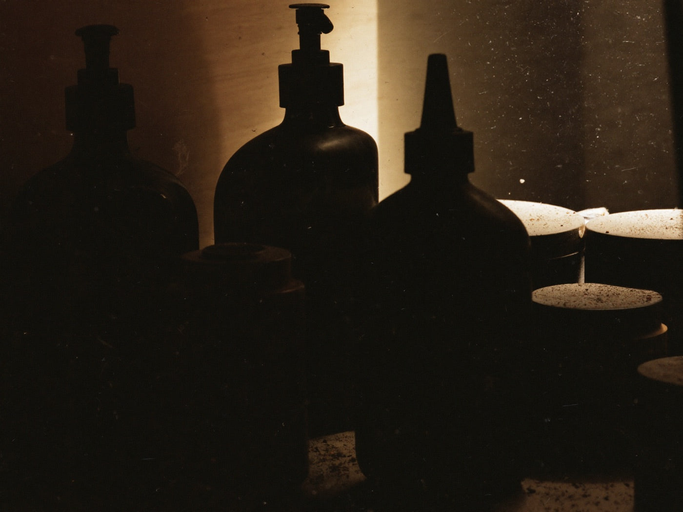 Half-used generic grooming bottles and a gummy jar as dark silhouettes shoved into the shadowed back of a bathroom cabinet
